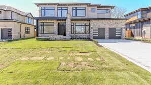 A modern two-story house with a large front lawn, a garage, and a driveway. - Luxury 5 BR, Gym, Sauna, Thtr, OD FP & Ktcn, Lake (Burlington)