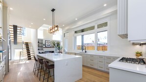 A modern kitchen with a central island, bar stools, a hanging light fixture, and a view of the backyard through large windows. - Luxury 5 BR, Gym, Sauna, Thtr, OD FP & Ktcn, Lake (Burlington)