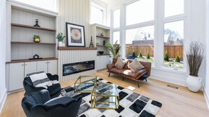 A spacious living room with a fireplace, a sofa, a coffee table, and a large window offering a view of the backyard. - Luxury 5 BR, Gym, Sauna, Thtr, OD FP & Ktcn, Lake (Burlington)