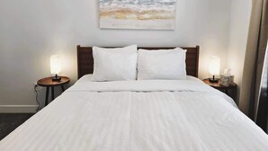 A neatly made bed with white linens, a wooden headboard, and two bedside lamps on matching nightstands.