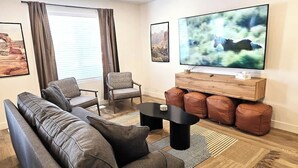 A modern living room with a sofa, armchairs, a coffee table, and a TV on a wooden stand.