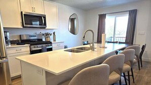 A modern kitchen with white cabinets, a stainless steel microwave, a double oven, and a large island with bar stools.