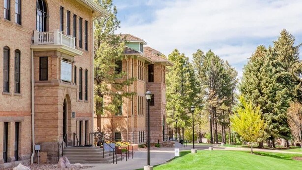A historic building with a brick facade, a balcony, and a well-maintained lawn with trees.