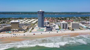 A coastal cityscape with a prominent tall hotel, a beach, and a marina.