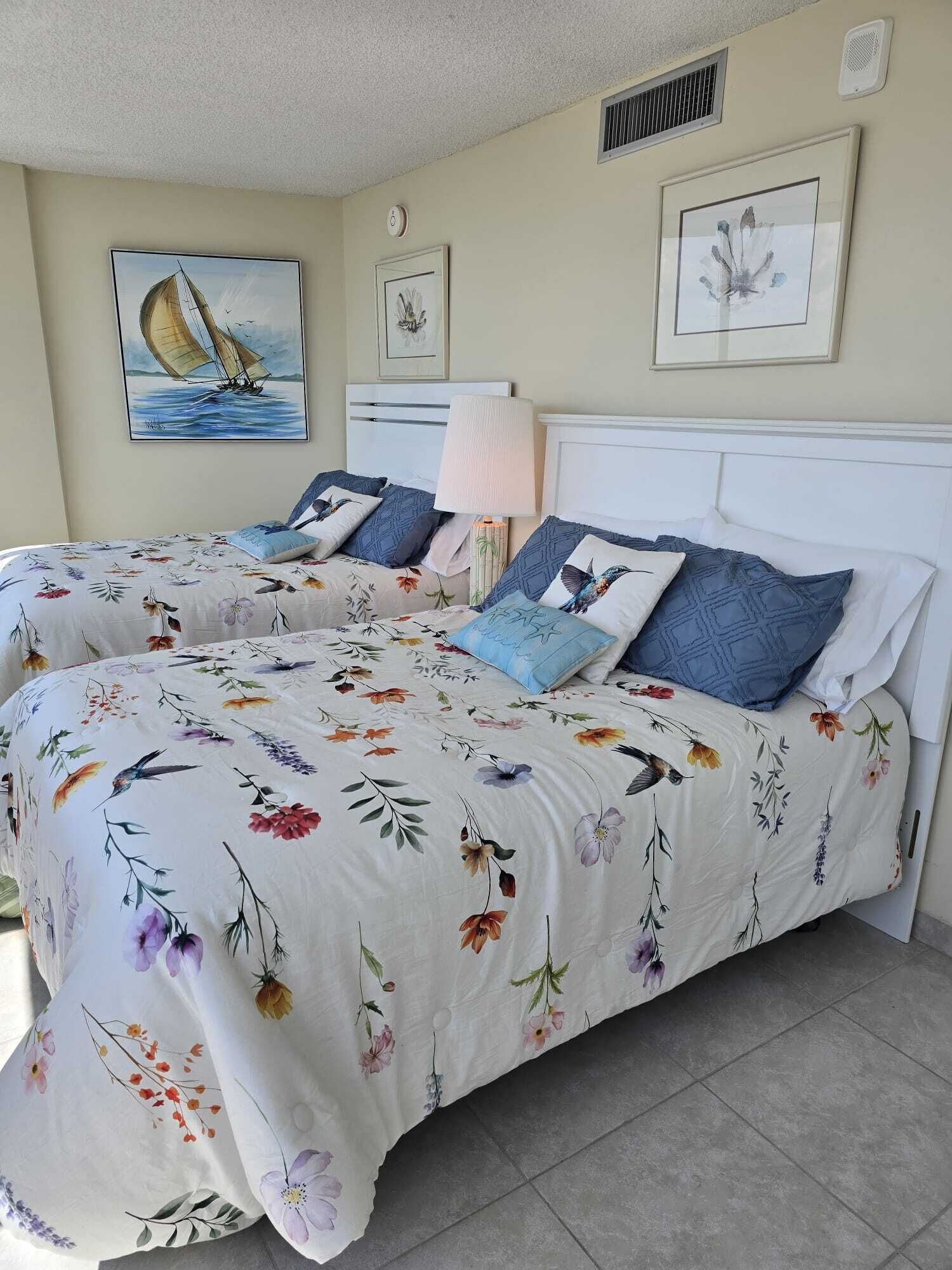 Ein Doppelbett mit Blumenmuster auf der Bettwäsche, eine Nachttischlampe und gerahmte Kunstwerke an den Wänden.