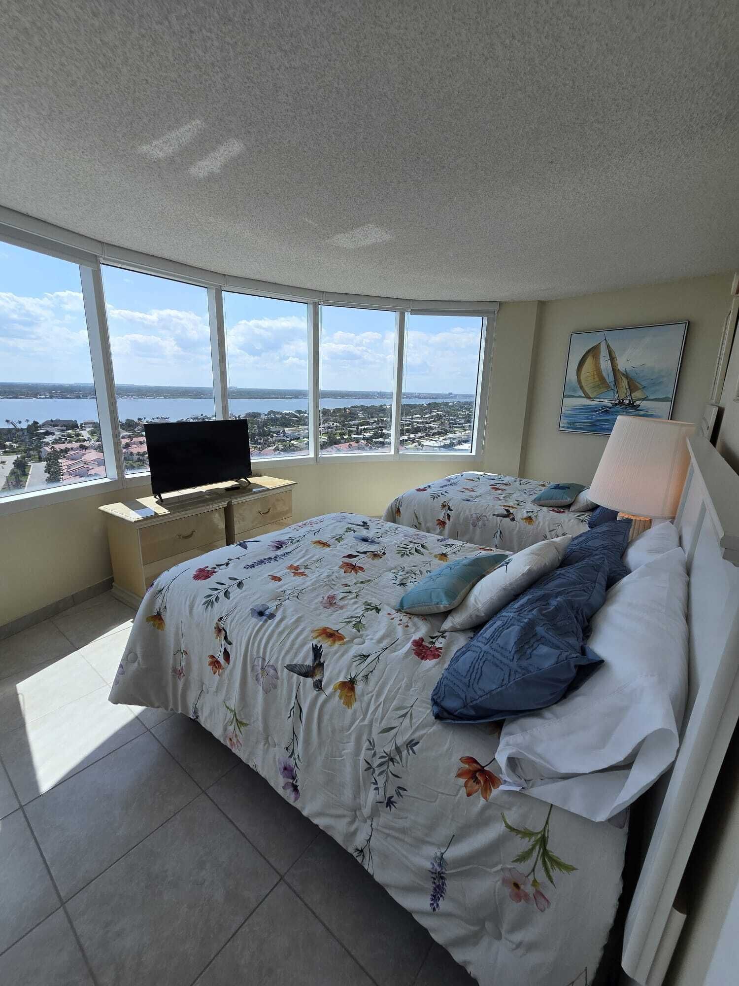 Un dormitorio con techo curvo, cama con ropa de cama floral, televisor sobre un mueble bajo y un ventanal con vista a la ciudad.