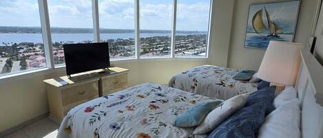 Un dormitorio con techo curvo, cama con ropa de cama floral, televisor sobre un mueble bajo y un ventanal con vista a la ciudad.