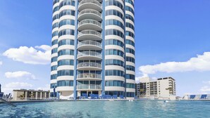 A tall, modern hotel with multiple balconies and a pool area in front.