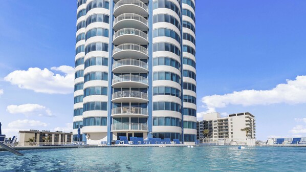 Een hoog, modern hotel met meerdere balkons en een zwembad ervoor.
