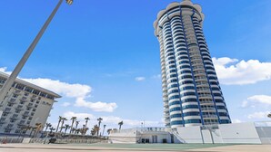 A tall, cylindrical hotel with multiple balconies, a flat roof, and a clear blue sky in the background.