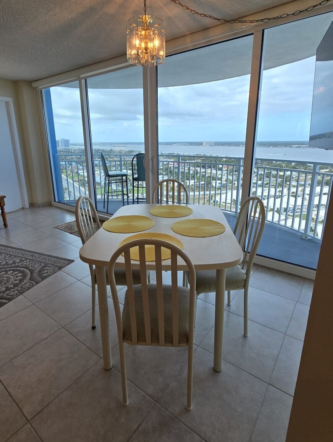 A dining area with a table and chairs, large windows with a view of the city and water, and a chandelier.