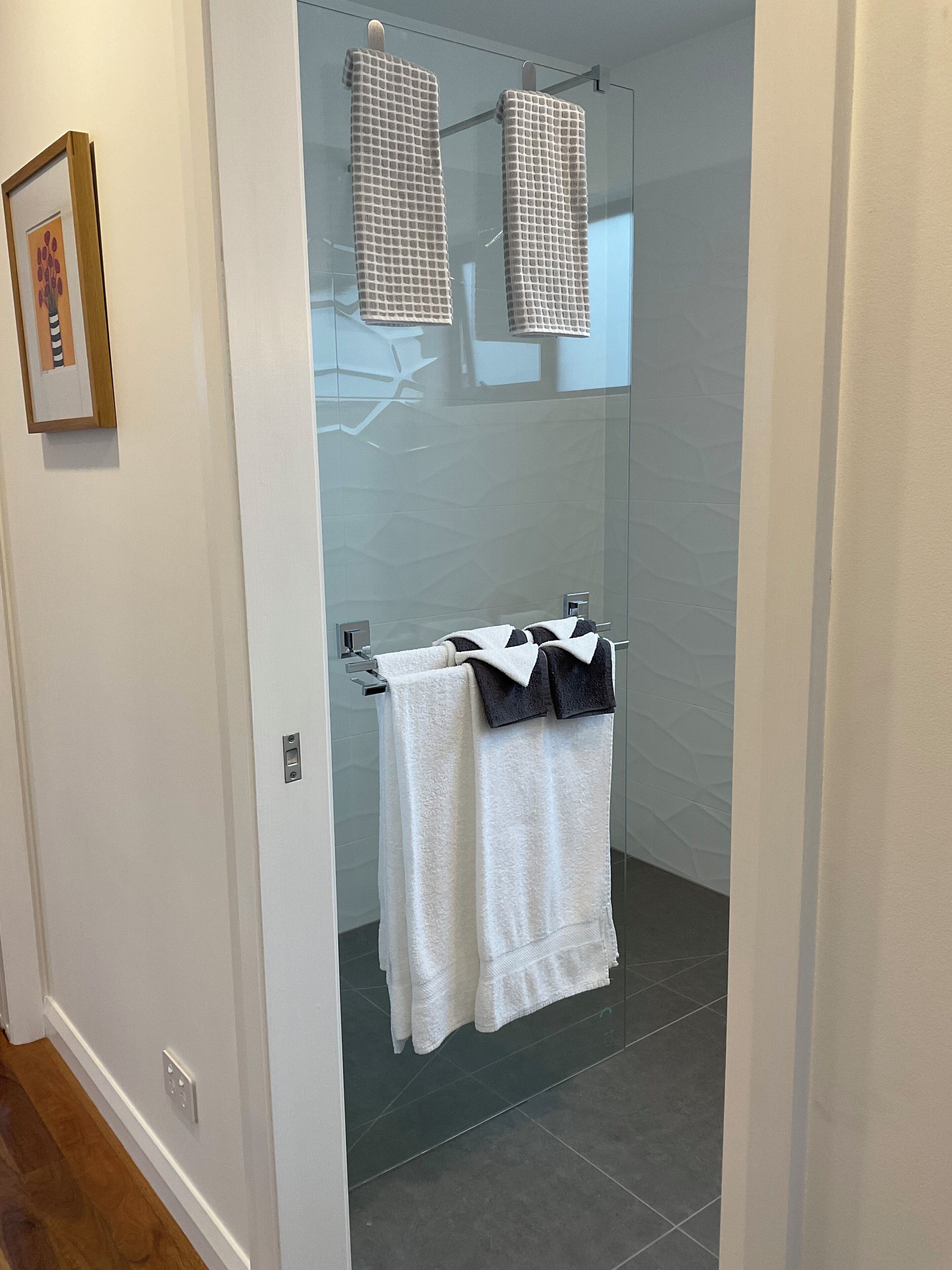 A modern bathroom with a glass shower enclosure, white tiled walls, and a wooden floor.