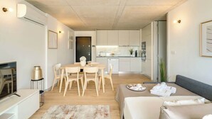 A modern living room with a sofa, a dining table with chairs, a TV, and a kitchen area in the background. - Balcony 2BRs with Pool & Parking by HostWise (Vila Nova de Gaia)