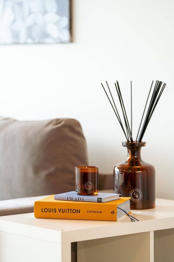 A small table with a book titled 'LOUIS VUITTON', a candle, and a vase with reed sticks.