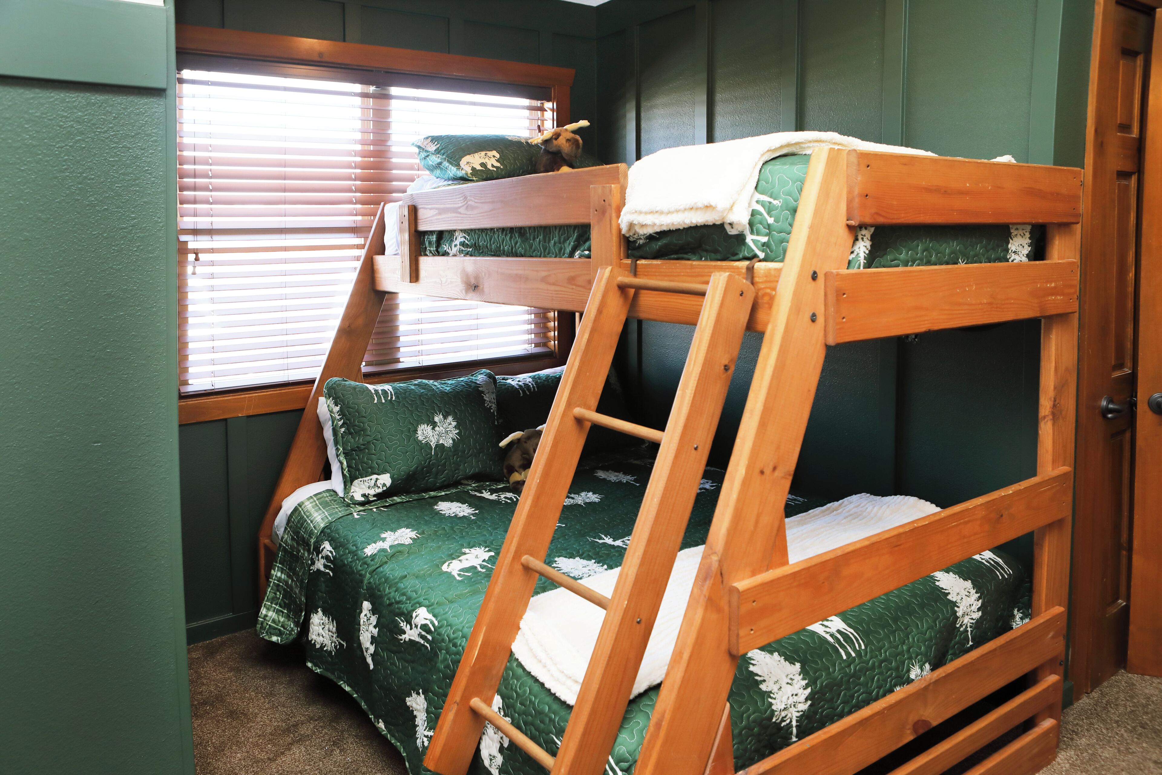 A bunk bed with a ladder, a window with blinds, and a door.