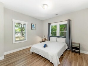 Une chambre à coucher avec un lit, deux fenêtres, une table de chevet et une commode.
