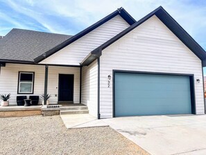 A modern two-story house with a garage, a front porch with outdoor seating, and a gravel driveway. - NEW! GameRm–HotTub–TheaterRm–Mtn Views–3000sf–BBQ (Spanish Valley)