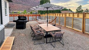 Eine Terrasse im Freien mit Grill, Tisch, Stühlen und einer Hängematte.