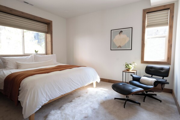 Un dormitorio con una cama, una silla, una mesita con una planta y un cuadro en la pared.