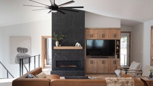 A modern living room with a fireplace, wooden cabinets, a large flat-screen TV, and a sofa. - Newly Built/Furnished Quiet Lux Ski-In/Out Hot Tub (Government Camp)