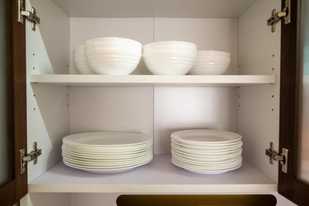 A cabinet with two shelves, each holding stacks of white plates.