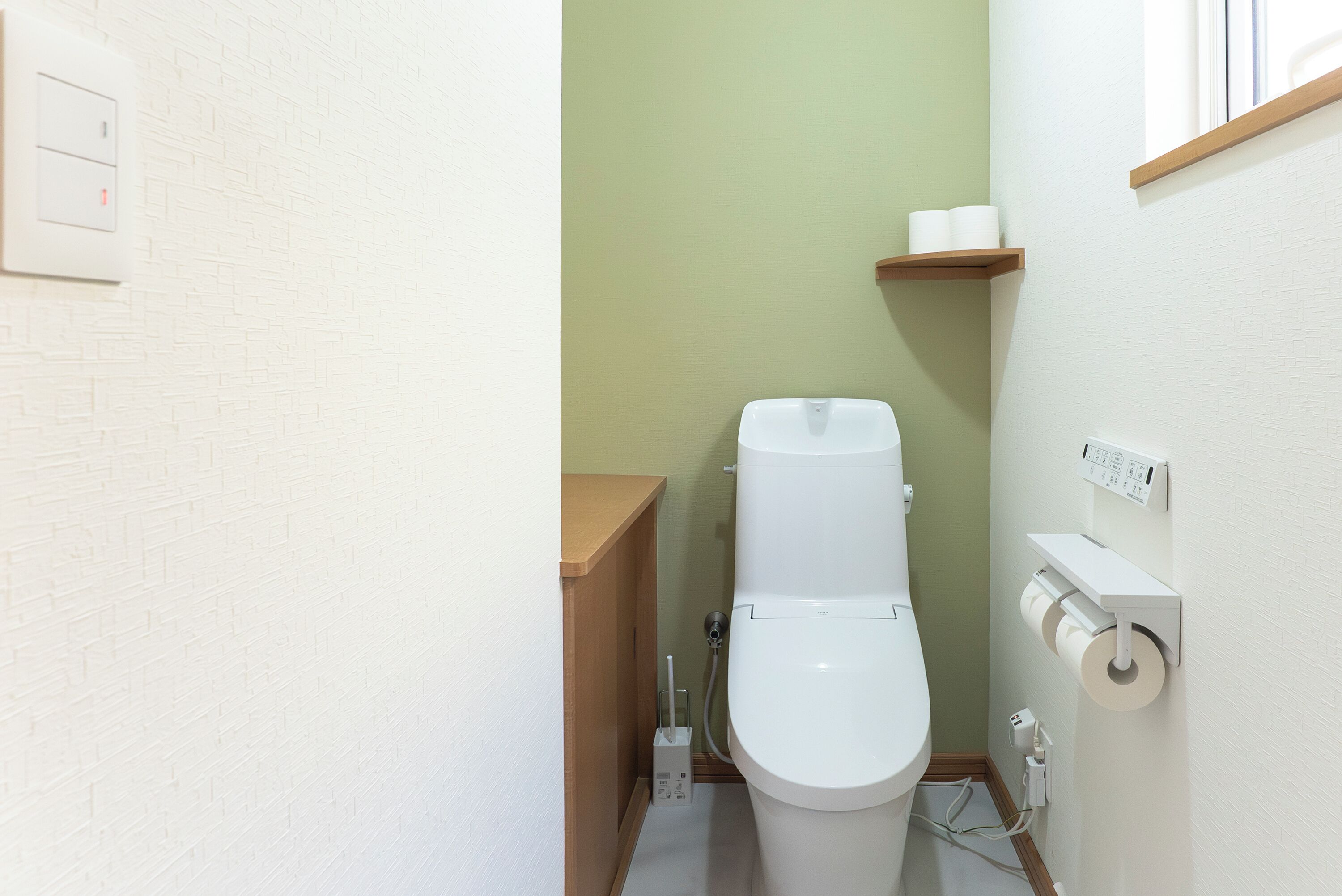 Un baño pequeño y limpio con inodoro, un armario de madera y una repisa con papel higiénico.