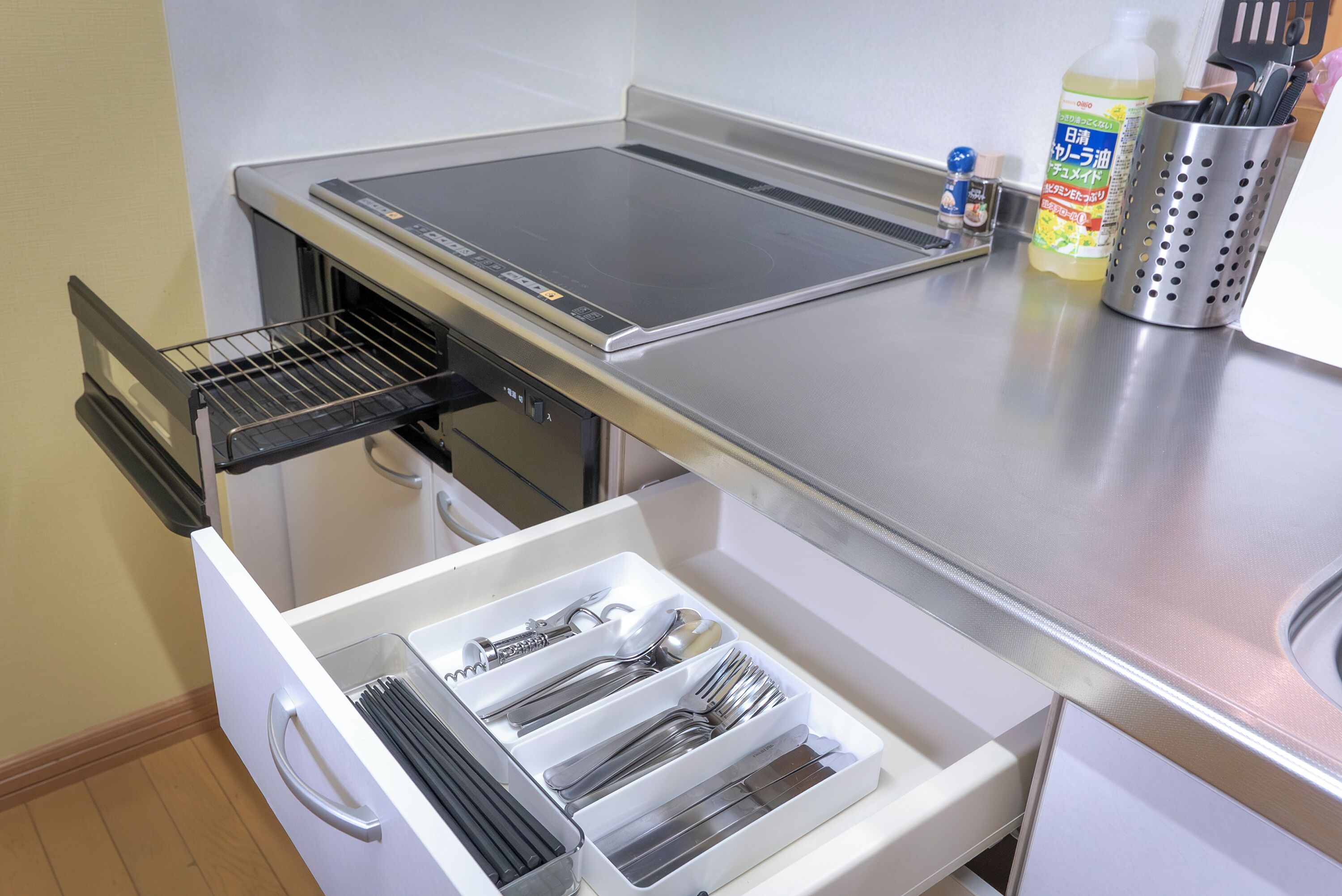 Una cocina con estufa integrada, un cajón con utensilios y una botella de detergente.