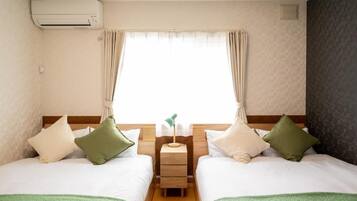 A hotel room with two beds, a bedside table, an air conditioning unit, and a window with curtains.