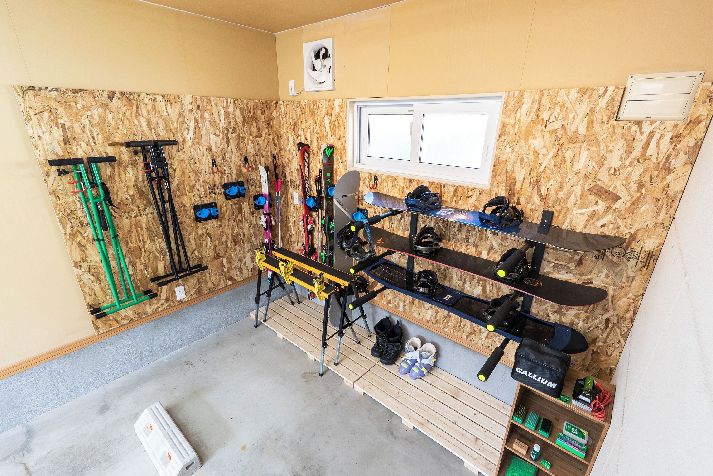 A ski storage area with racks for skis and snowboards, a bench, and a shelf with ski boots and equipment.