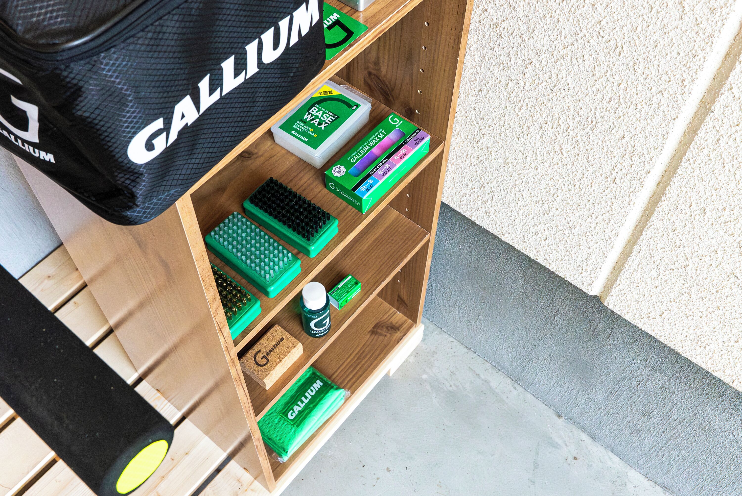 A wooden shelf with various items including a black bag labeled 'GALLIUM', a green box labeled 'GALLIUM', and a green sponge.