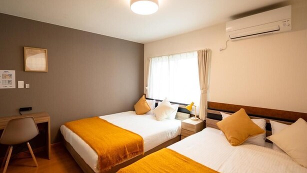 Ein Hotelzimmer mit zwei Betten, einem Schreibtisch und einer Klimaanlage.
