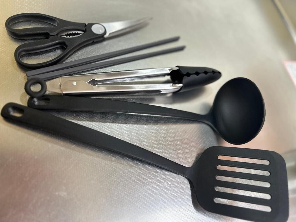 A set of kitchen utensils including scissors, tongs, and a spatula on a metallic surface.