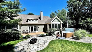 A two-story house with a stone patio, a covered outdoor seating area, and a fire pit.