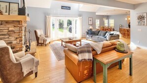 A spacious living room with a stone fireplace, a sofa, a coffee table, and a dining area in the background.