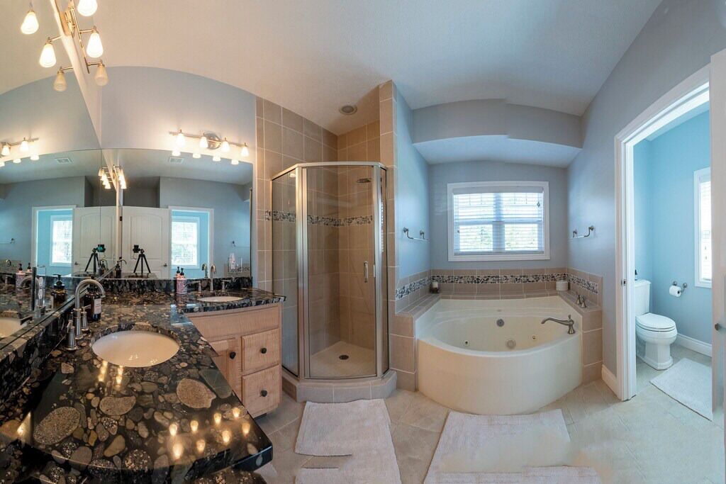 Een badkamer met een grote spiegel, twee wastafels, een douche en een bad.