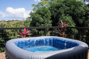 Una bañera de hidromasaje inflable sobre una terraza de madera, con vistas a exuberante vegetación y colinas al fondo.