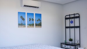 Un dormitorio con cama, aire acondicionado, estante en la pared y fotografías enmarcadas.