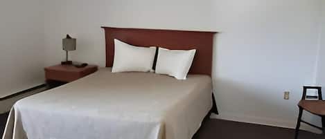 Un dormitorio con cama, mesita de noche, silla y lámpara.
