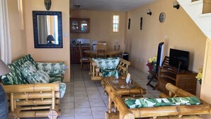A living room with a sofa, a coffee table, and a television. There is a kitchen in the background. - Marvelous 2-bedroom apartment with AC (Grenadines)