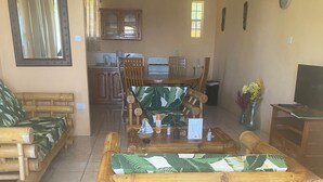 A living room with a central wooden coffee table, a sofa with a green leaf pattern, and a television on the right. - Marvelous 2-bedroom apartment with AC (Grenadines)
