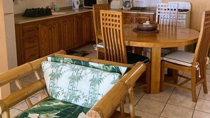 A compact kitchen with wooden cabinets, a microwave, a gas stove, and a dining area with wooden chairs and a table. - Marvelous 2-bedroom apartment with AC (Grenadines)