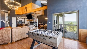 A modern living room with a foosball table, a cozy seating area, a kitchen, and a balcony with a scenic view. - 7 Springs Mountain Ski-In | Sauna + Game Room (Champion)