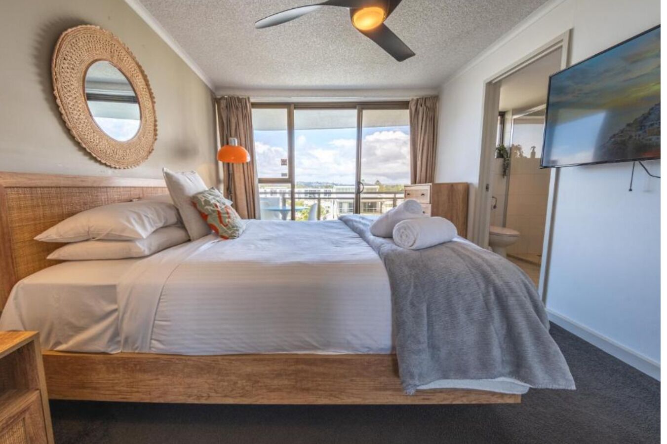 Une chambre d’hôtel avec un grand lit, un ventilateur de plafond, une télévision et une vue sur la ville.