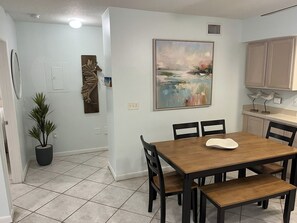 A dining area with a wooden table and chairs, a painting on the wall, and a potted plant. - Spacious Beachside Condo in Cocoa Beach, Florida! 125 Feet to Beach! (Cocoa Beach)