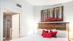 Un dormitorio con una cama grande, ropa de cama blanca, cabecero de madera y un cuadro con árboles y flores en la pared.