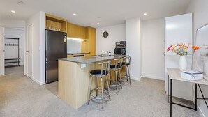 A modern kitchen with a central island, bar stools, a refrigerator, and a coffee machine.