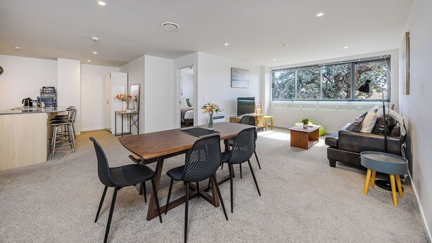 A modern living room with a dining area, a sofa, and a large window with a view of trees.