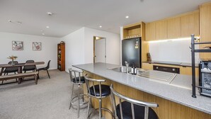 A modern kitchen with a bar area, a dining table with chairs, and a wooden cabinet.