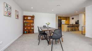 A modern living room with a dining area, a bookshelf, and a kitchen in the background.