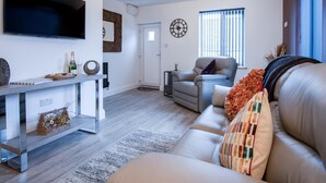 A modern living room with a flat-screen TV, a grey sofa, a recliner, and a coffee table.